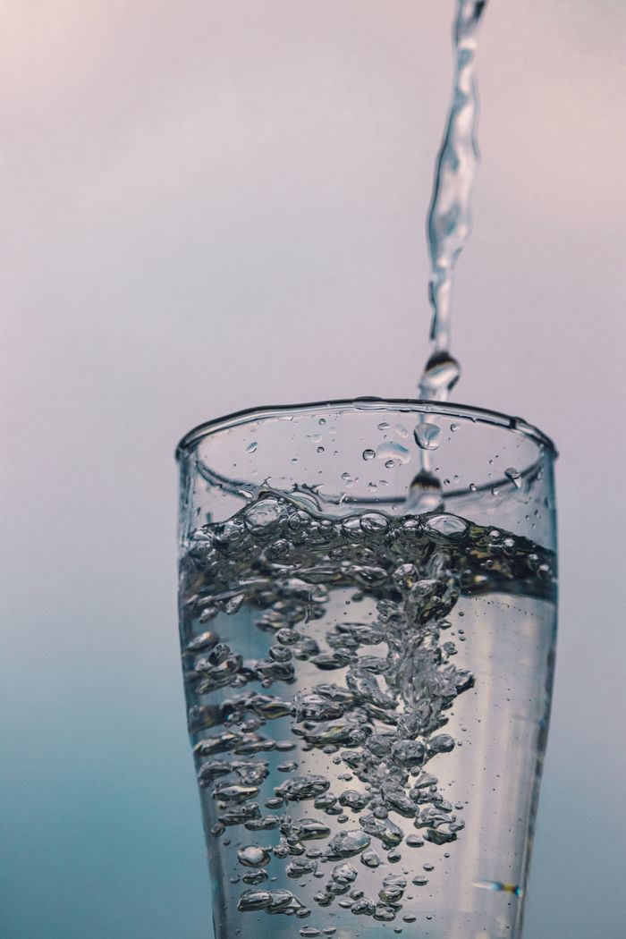 Low angle of transparent glass with bubbles of pouring cold water against blurred colorful background